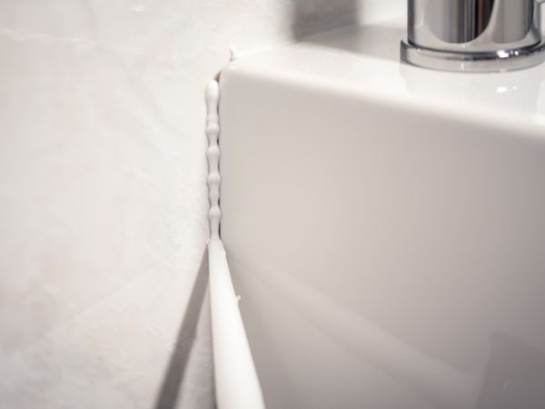 A close-up view of a bathroom sink corner sealed with Soudal silicone, showcasing a clean and effective seal for sanitary applications.