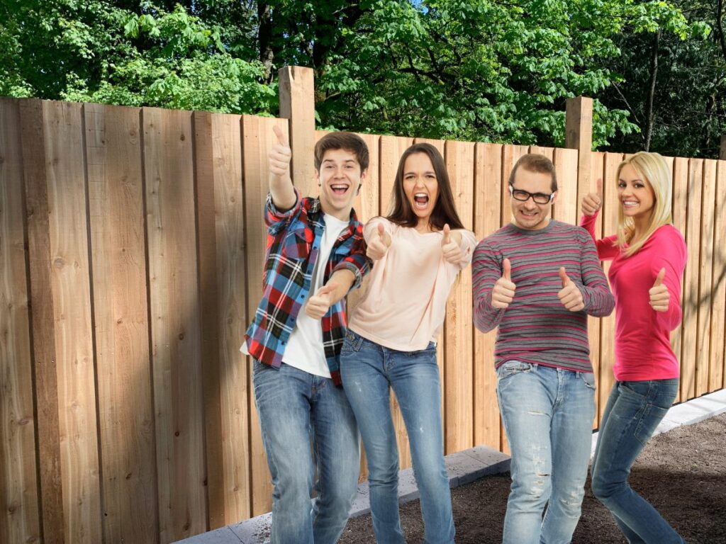 Four happy people giving thumbs up in front of a newly repaired timber fence in Busselton