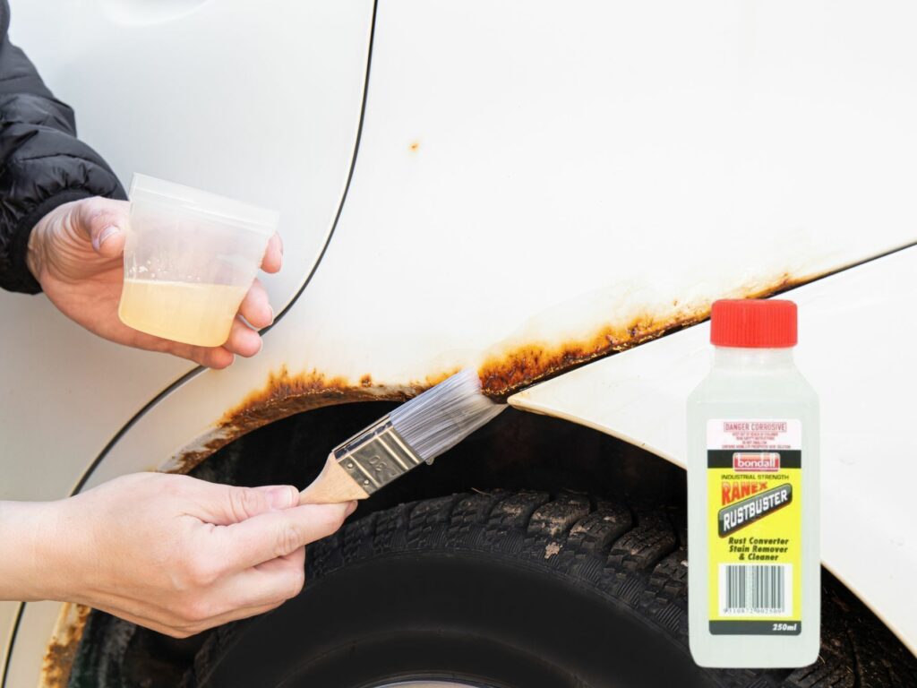 Person applying Ranex Rustbuster to a rusted car wheel arch with a paintbrush, showing step-by-step DIY rust removal in action.