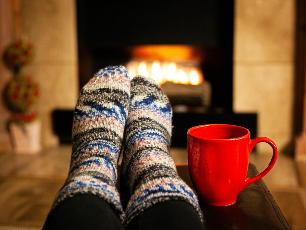 Cosy winter socks and red mug in front of a lit fireplace in a Busselton home, representing comfort during winter preparation.
