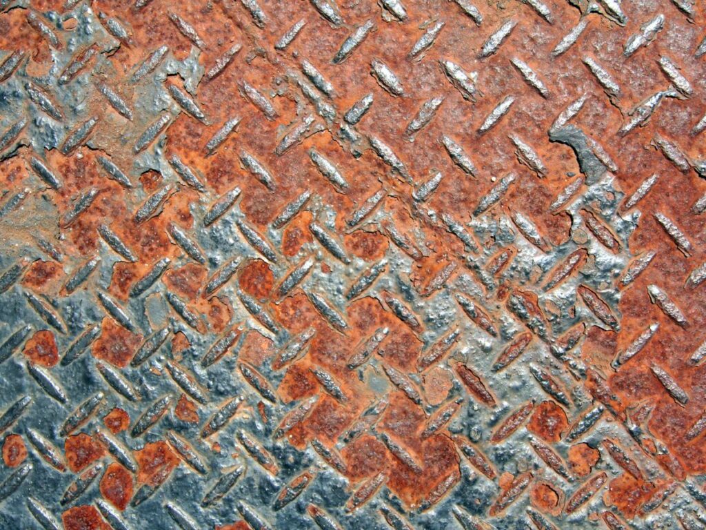 Close-up of heavily rusted metal checker plate surface, showing corrosion damage and the need for rust treatment or restoration.