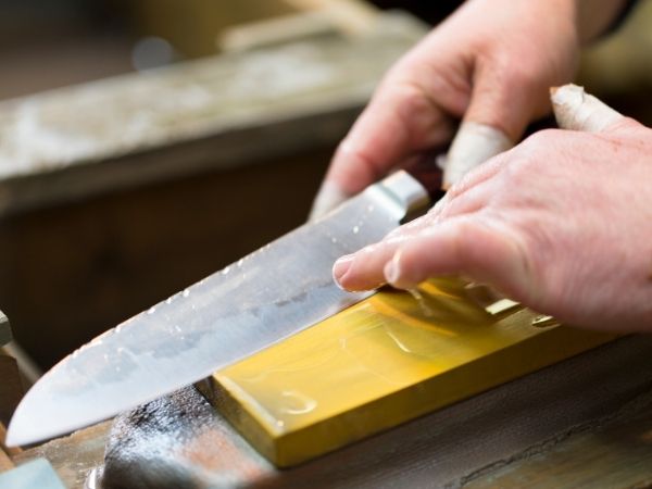 Close-up of hands sharpening a kitchen knife on a yellow whetstone for precision edge maintenance