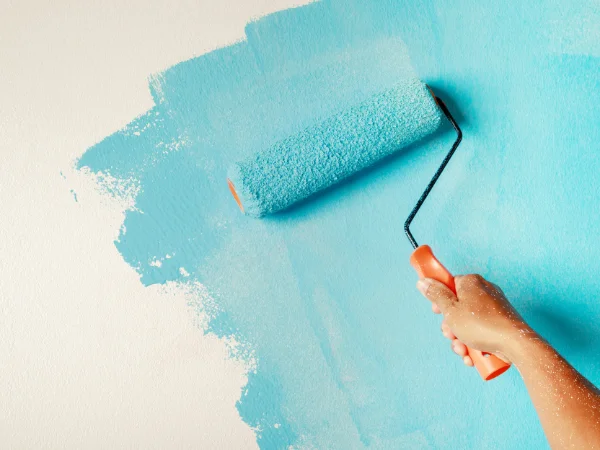Roller applying blue paint evenly across an interior wall. Feature Image for our Painting Tips Blog Post.