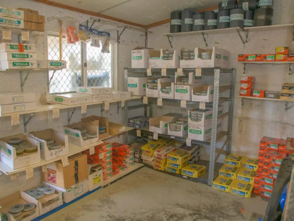 An indoor trade stockroom at a hardware store featuring steel shelving units and pegboard walls neatly packed with storage bins and boxes of bulk fasteners, screws, and building fixings.