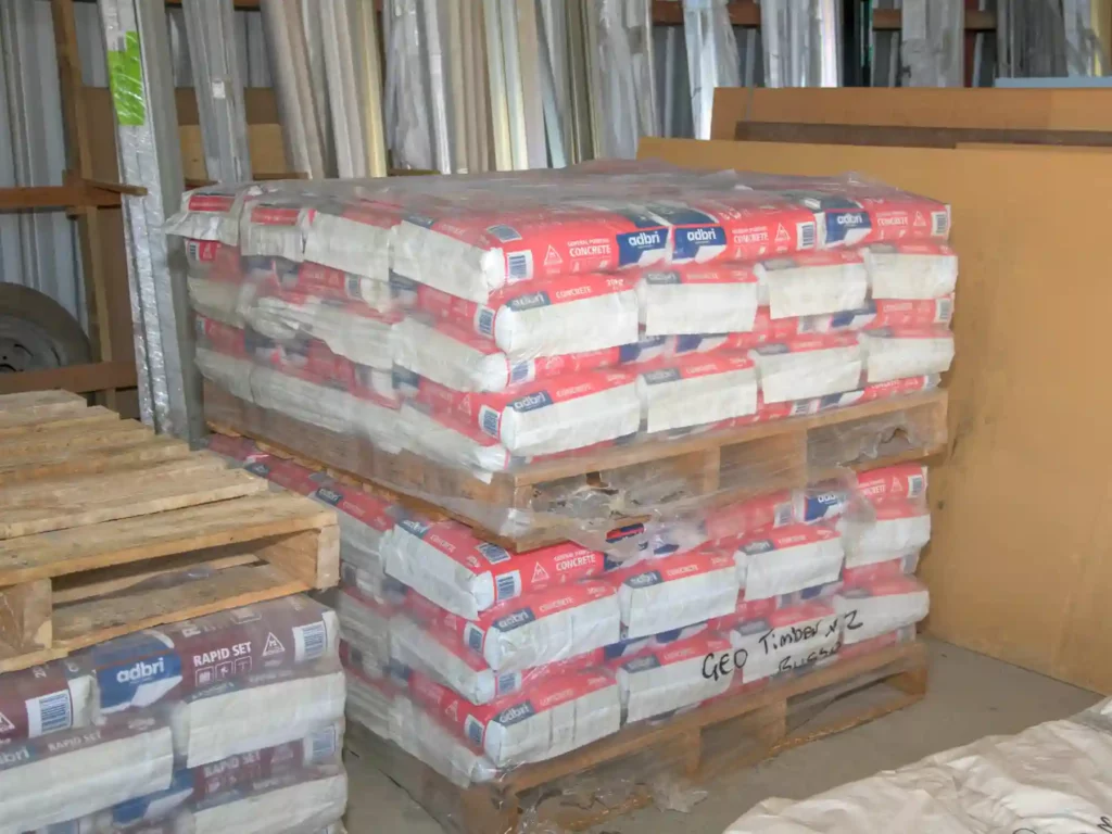 Multiple heavy plastic-wrapped wooden pallets stacked high with bulk bags of Adbri concrete mix inside a commercial building supply warehouse.
