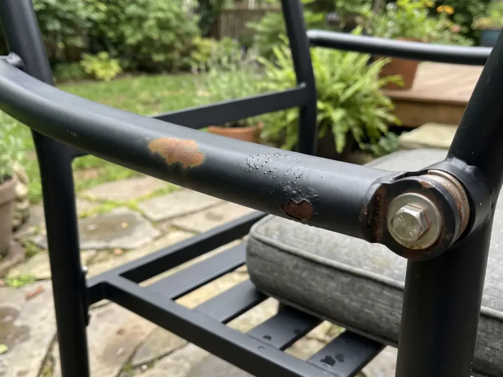 Early signs of rust on an outdoor chair frame, surface bubbling and pitting around a bolt.